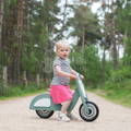 Toddler sitting on green Montessori Balance Vespa with the forest behind her. 