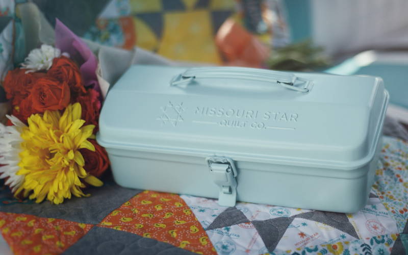 a close-up of the turquoise metal toolbox that contains jenny doan's signature quilting tools.