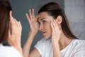 woman looking at her skin in the mirror at fines lines and wrinkles