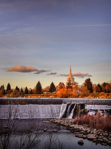 Idaho Falls temple surrounded by orange trees. Waterfalls in the foreground.