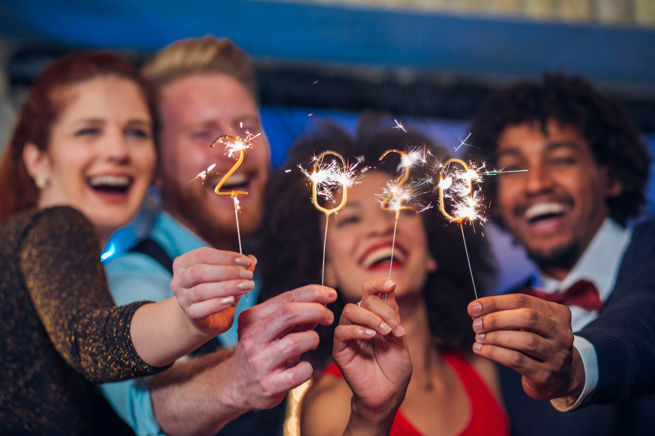 Several friends laugh while holding sparklers in front of them in the shape of numbers 2020.