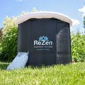 A Zenpod cold plunge tub stands against a background of green plants and grass