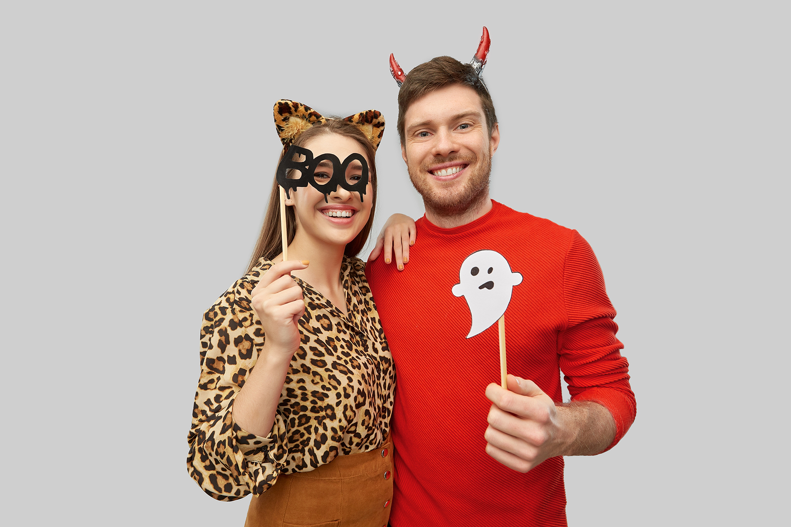A happy and smiling couple in halloween costumes of devil and leopard with party accessories over grey background