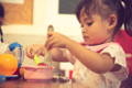 Little girl scooping food with fork and a knife.