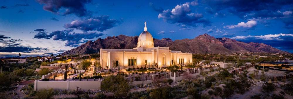 Panoramic photo of the Tucson Temple glowing against the mountains and evening sky.