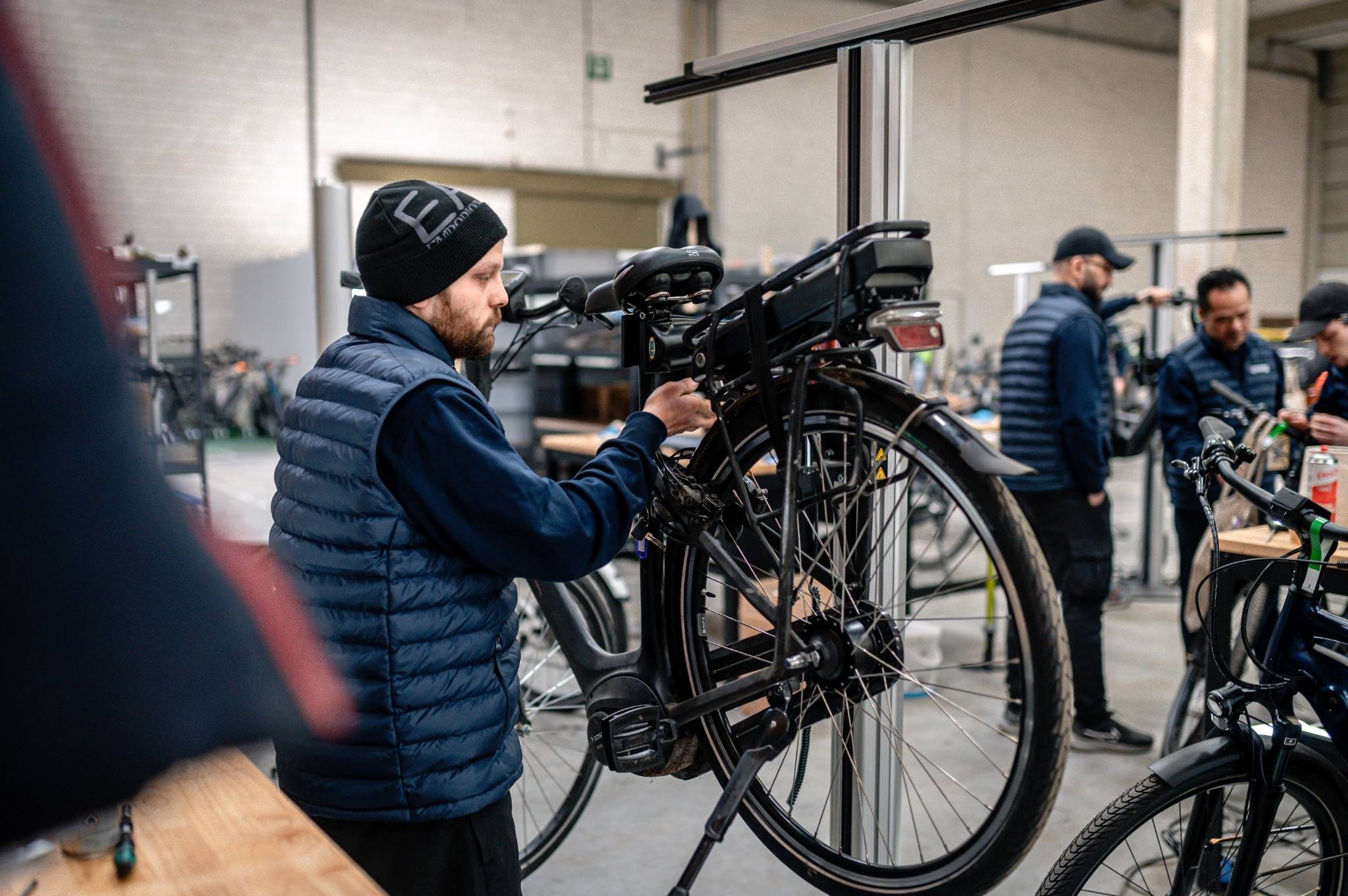 Monteur inspecteert accu en achterwiel van een elektrische fiets in professionele werkplaats voor onderhoud en controle.