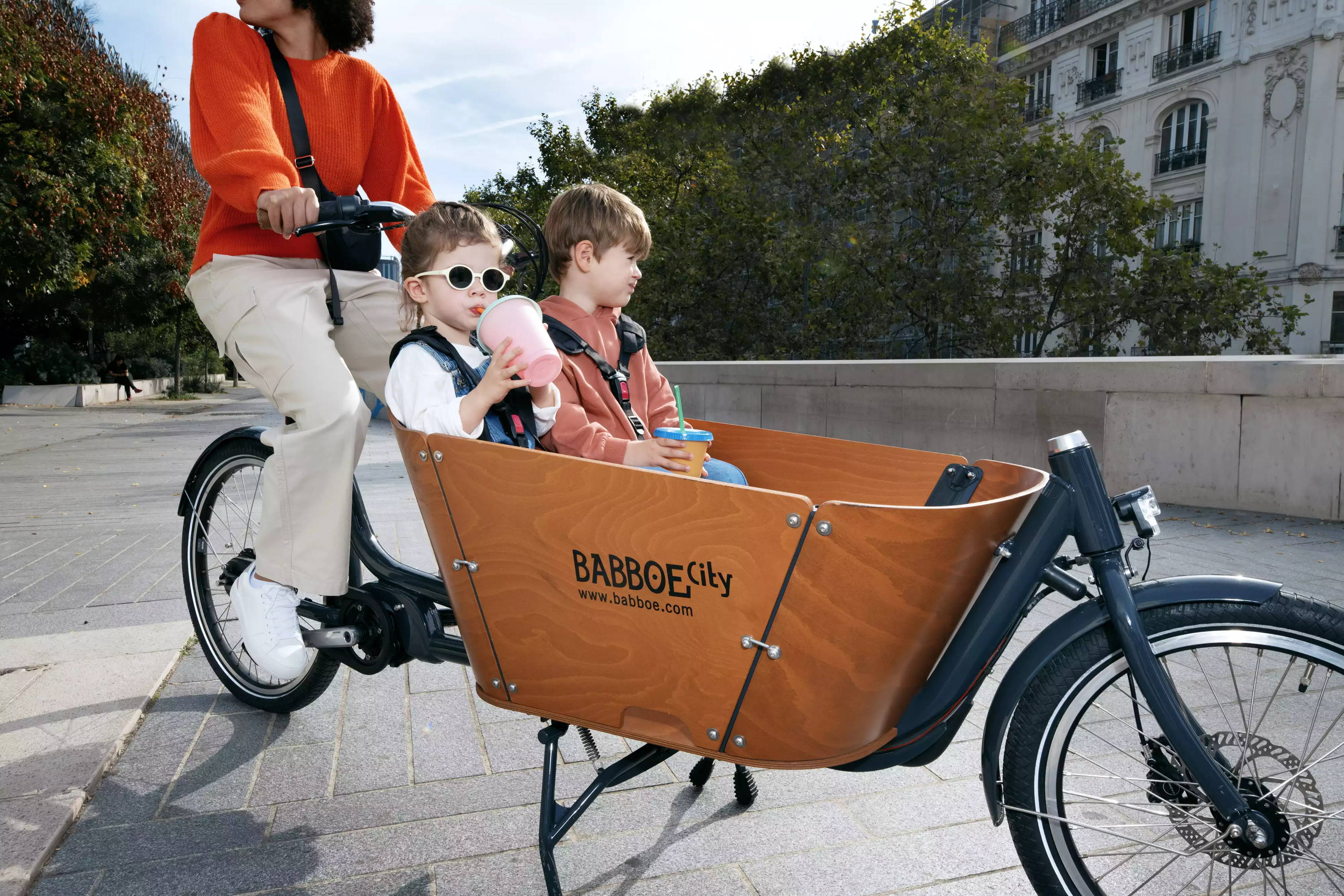 Deux enfant dans un vélo cargo électrique conduit par leur mère.