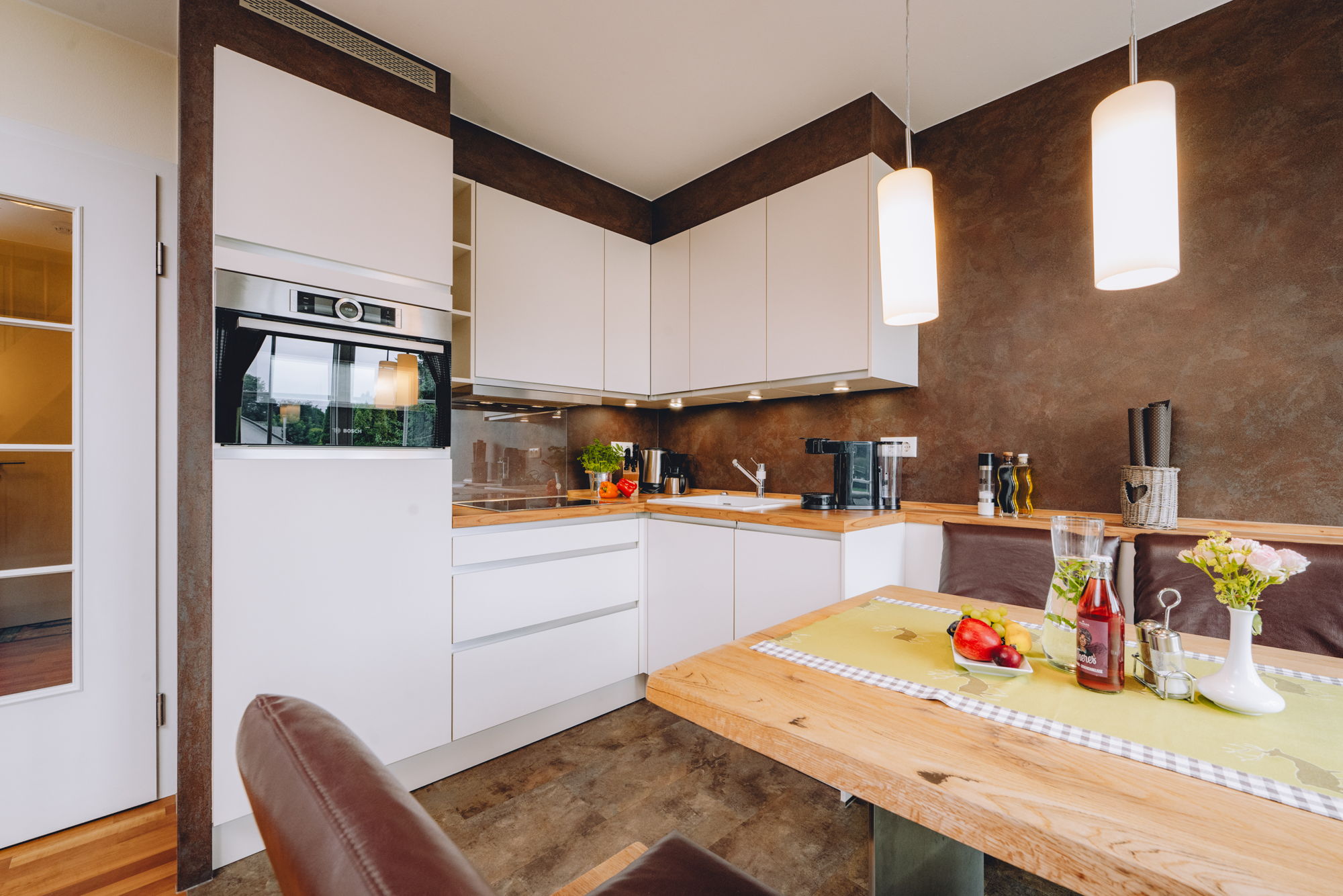 Eine moderne Küche mit weißen Schränken, einem Ofen und dunklen Wänden, im Vordergrund ein Holzesstisch.