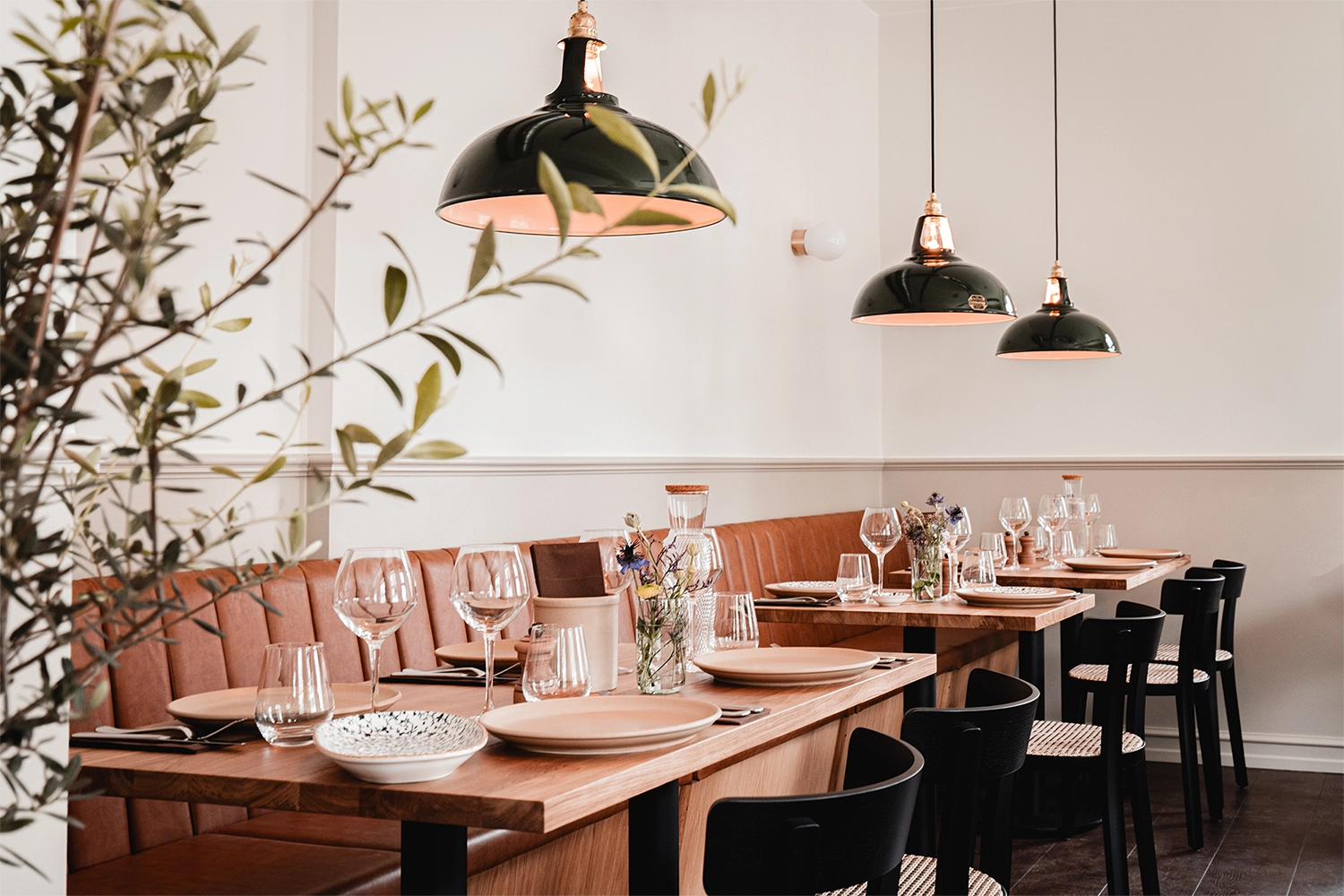Three large green Coolicon Lampshades hanging over wooden nordic restaurant tables and chairs with white walls. 