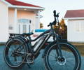 Vélo électrique qui sort du garage avec la maison et une voiture derrière