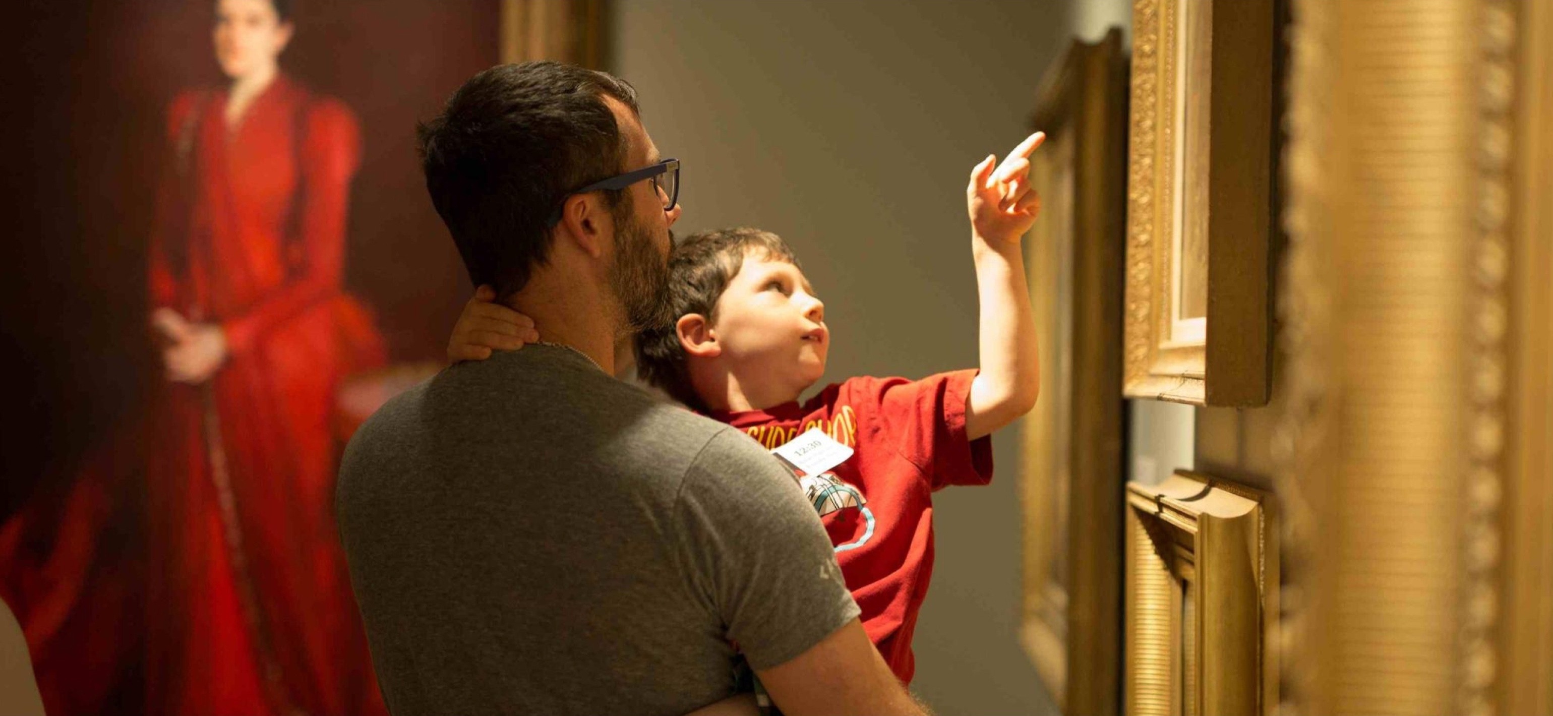 man holding a child and pointing at three paintings on the wall at the san antonio museum of art