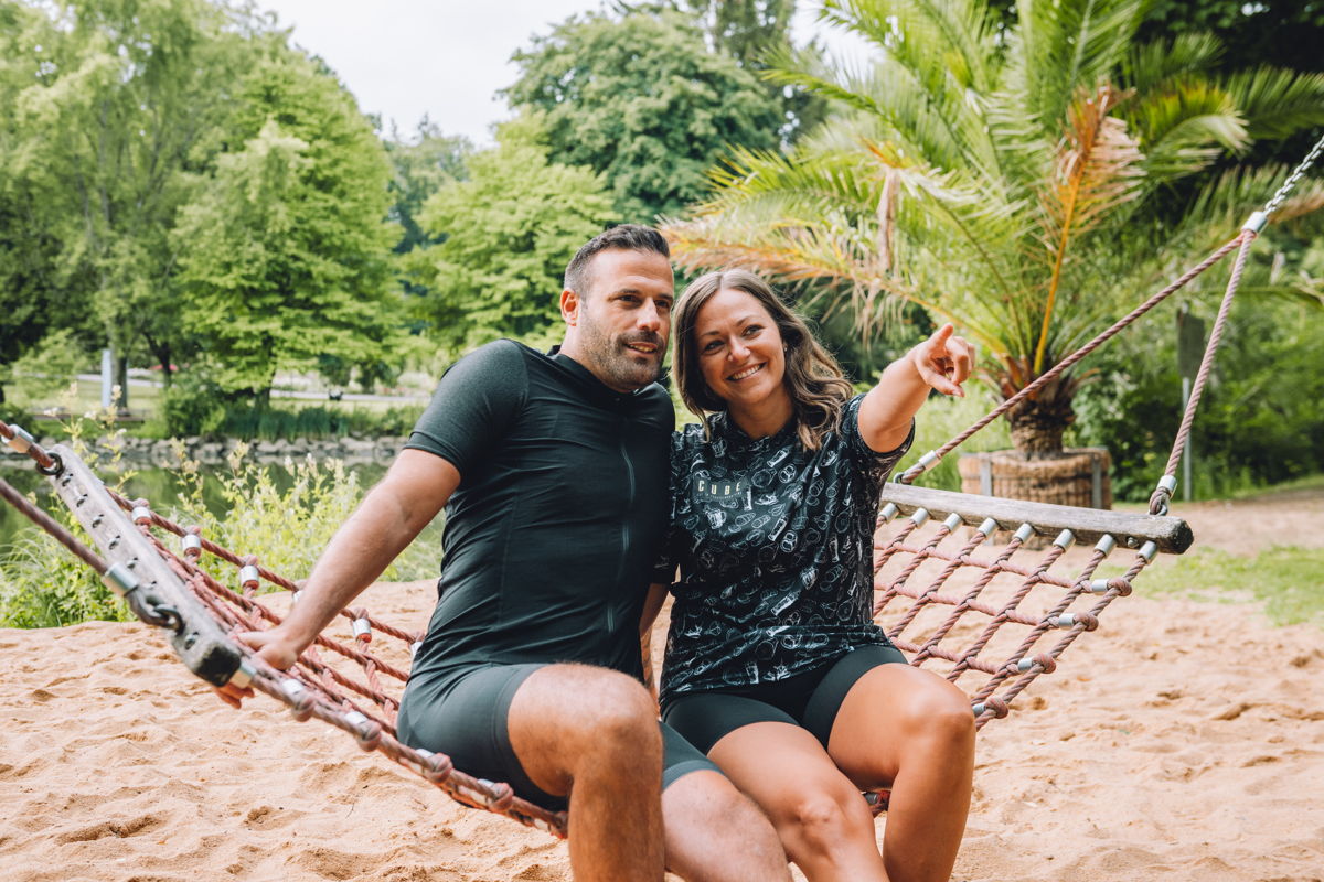 Ein Pärchen in Radbekleidung ruht sich auf einer Netzschaukel aus.