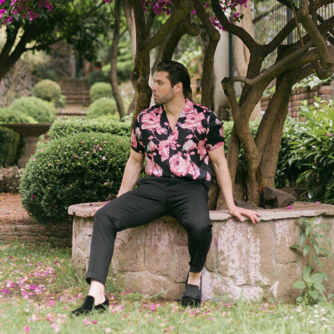 man sitting in the garden wearing black velvet shoes black pants and a black floral short sleeve silk shirt