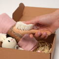 Woman's hand holding a wooden brush above the Montessori Baby Shower Gift box.