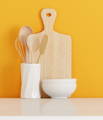 wooden cutting board and cooking utensils in a white ceramic container with two white bowls on a yellow background