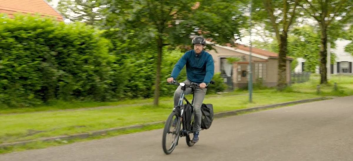 Cycliste avec casque roulant en speed pedelec avec sacoche dans une rue résidentielle arborée