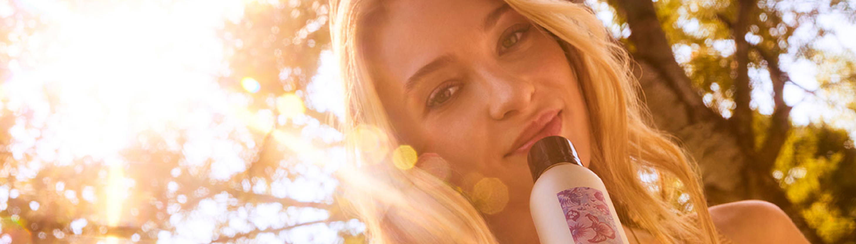 Blonde woman holding Davines More Inside styling product in the sunshine