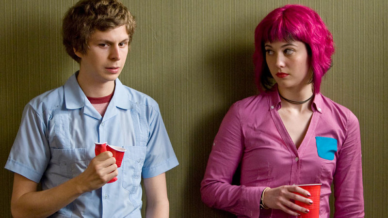 Scott and Ramona standing against a green wall. Scott is crushing a red drinking cup in his hands, Ramona looks at him with calm expression.