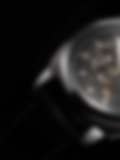 A close-up photo of a silver mechanical wristwatch with a black leather band