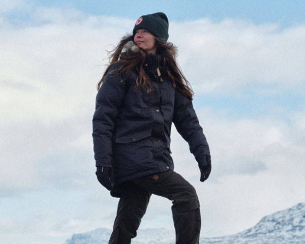 Woman wearing dark blue insulated and waterproof parka jacket in the snow from sustainable outdoors brand Fjällräven