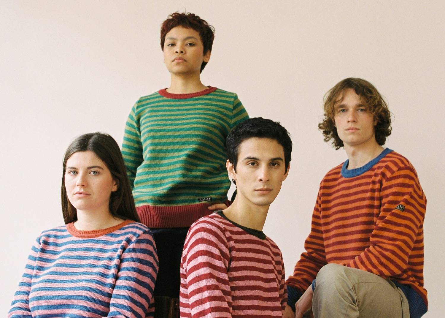 four people wearing the same sweater but in different colors sitting looking at the camera