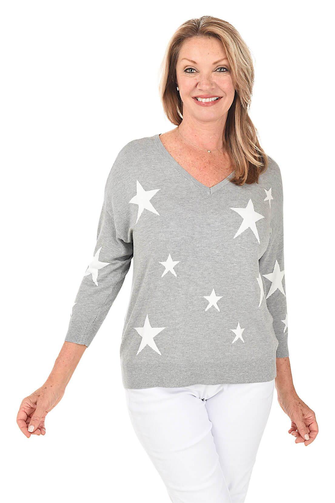 A woman wearing a grey and white star printed sweater and white pants