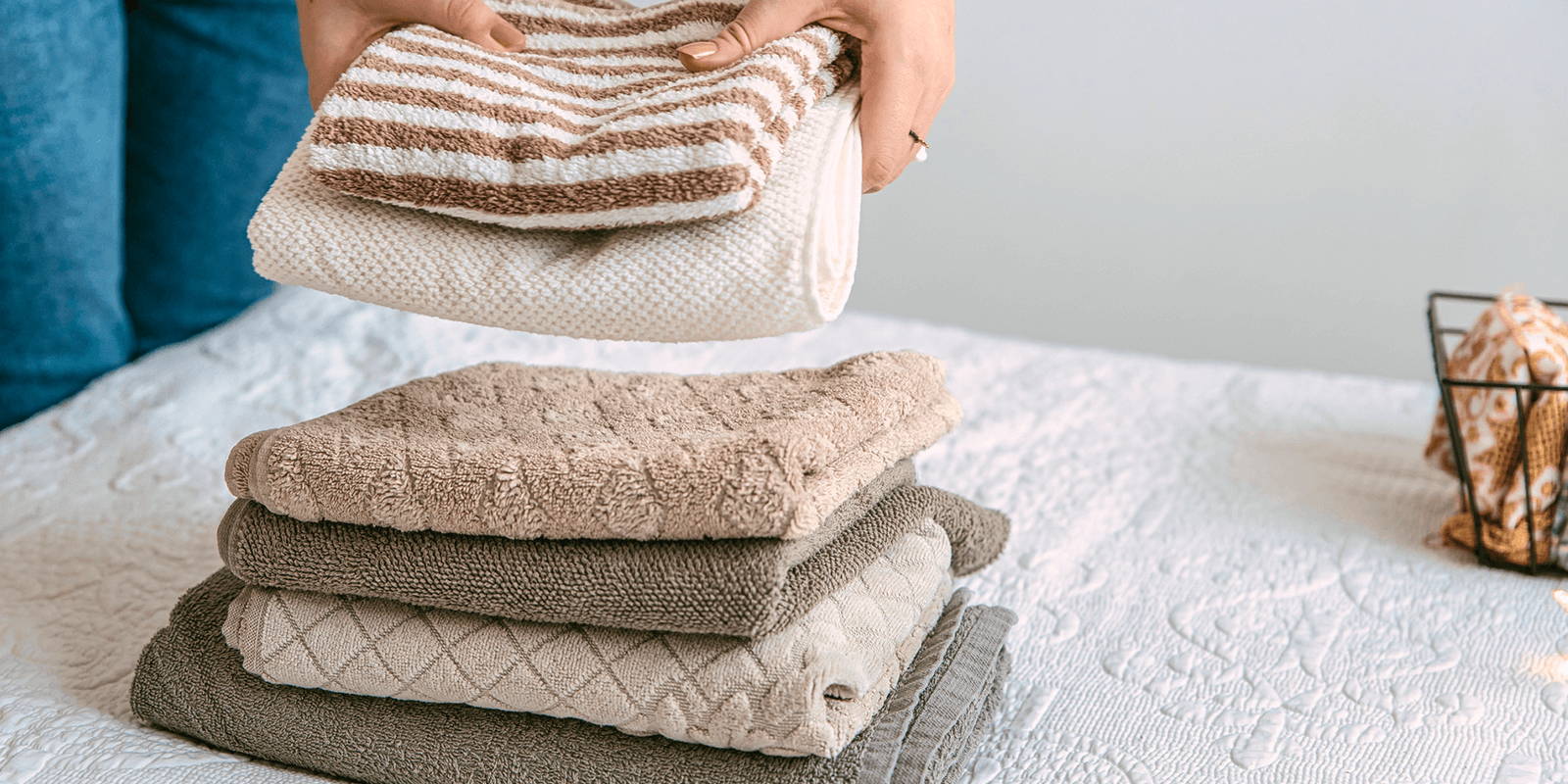 Hands setting folded towels on bed.