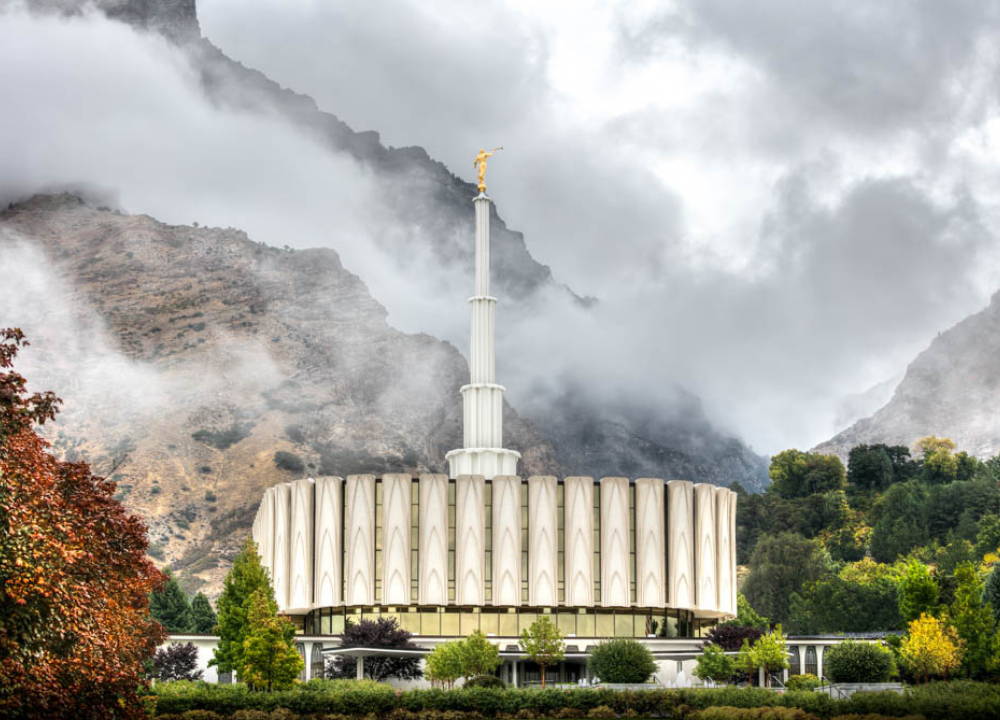 Provo Temple standing tall in front of cloudy mountains.