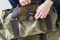 man sititng down pulling his passport out of the side pocket of an explorer duffel