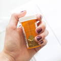 Womans hand holding an orange pill bottle being used as a makeshift weed grinder by shaking it with a coin inside