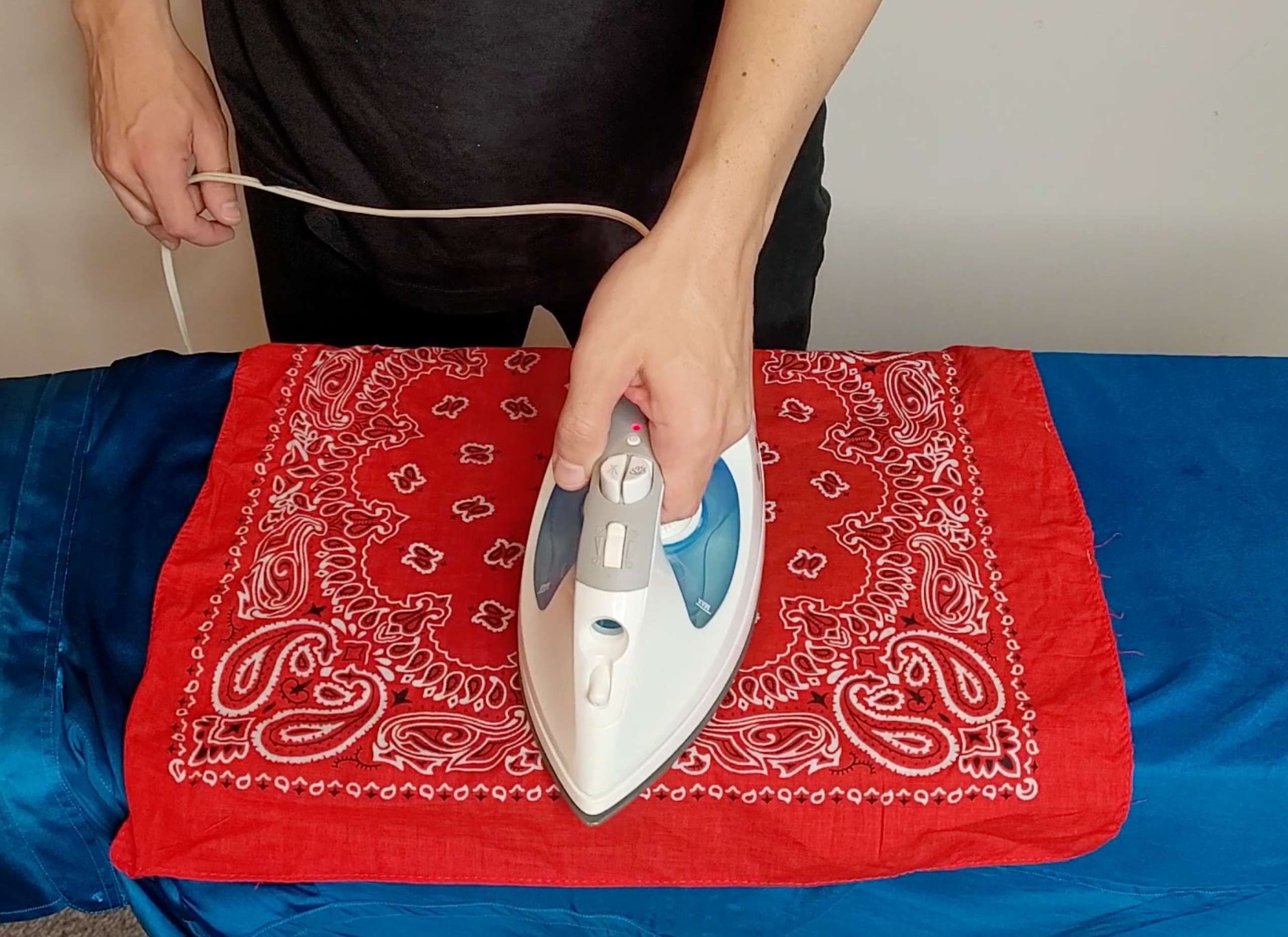 a photo of a man ironing a blue silk shirt using an iron and a thin cotton press cloth