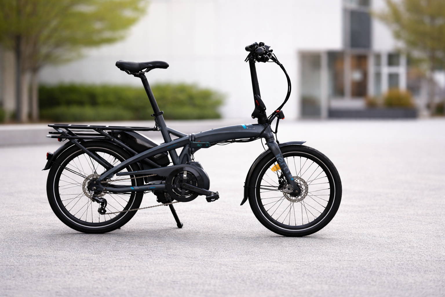 Compacte elektrische vouwfiets met lage instap, middenmotor en bagagedrager, zijaanzicht op straat met stedelijke achtergrond.