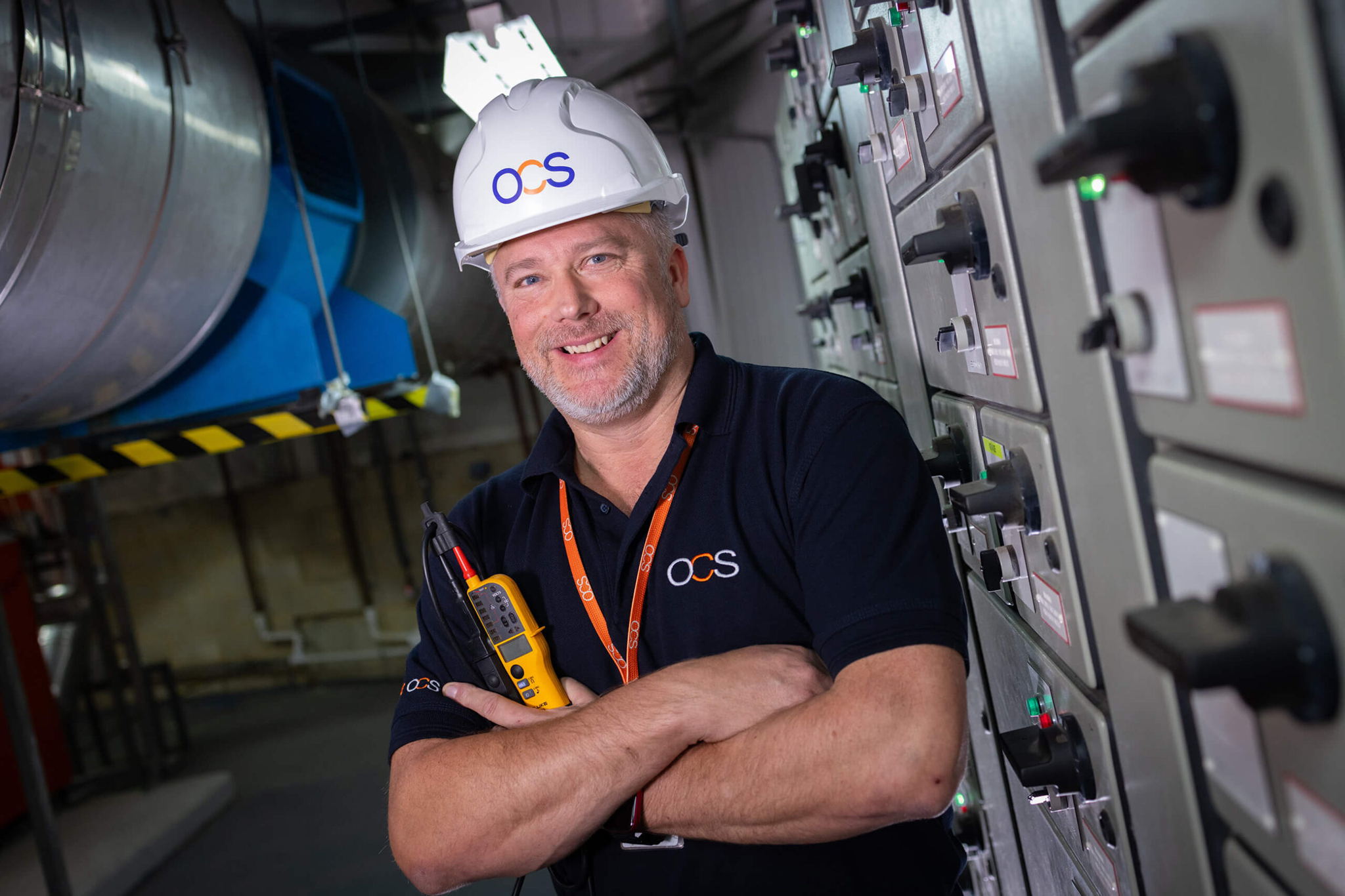 A man in a hard hat, representing an OCS hard services colleague, stands confidently at a construction site.