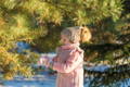 Little girl in cozy winter clothing standing next to a pine tree.