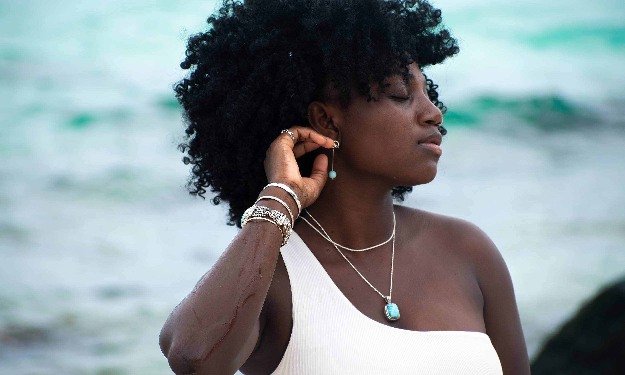 A woman next to the ocean wears pendants and chains.