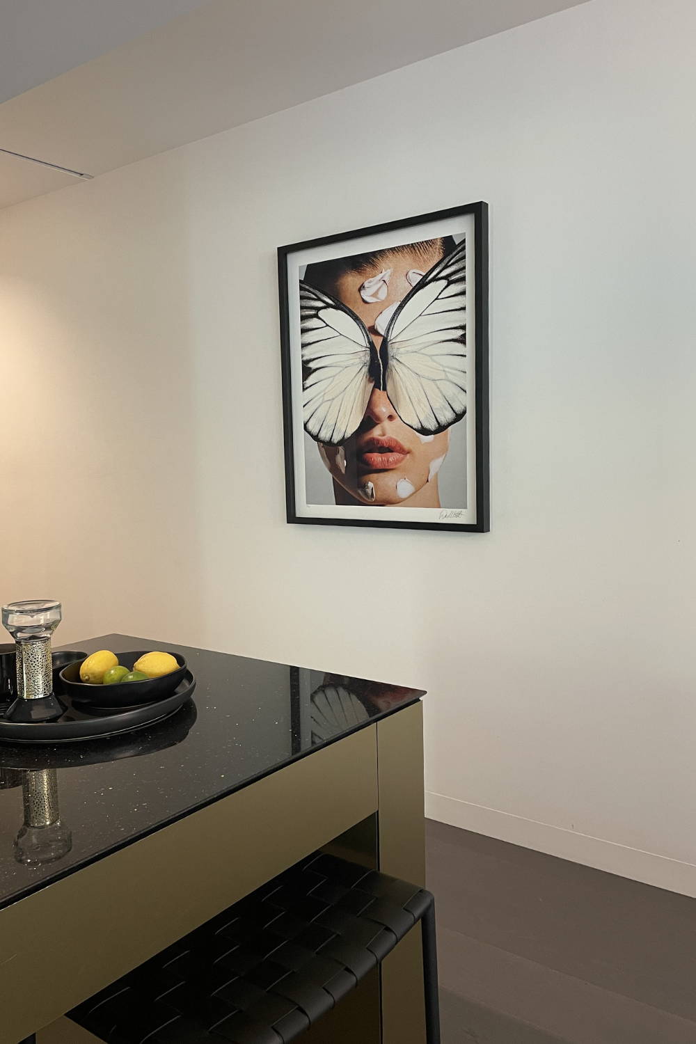 'Broken Wings White' by Dina Broadhurst - A collage-style art print of a girl with butterfly wings over her face, framed in black and styled in a stylish kitchen interior