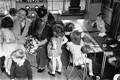 Maria Montessori sitting and talking to a little girl in a classroom full of children. 