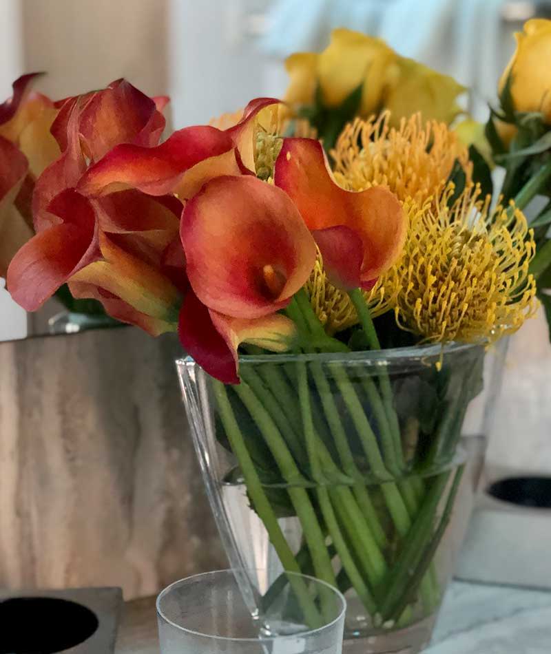 Orange and yellow arrangement of Calla Lilies and Pincushion next to a mirror