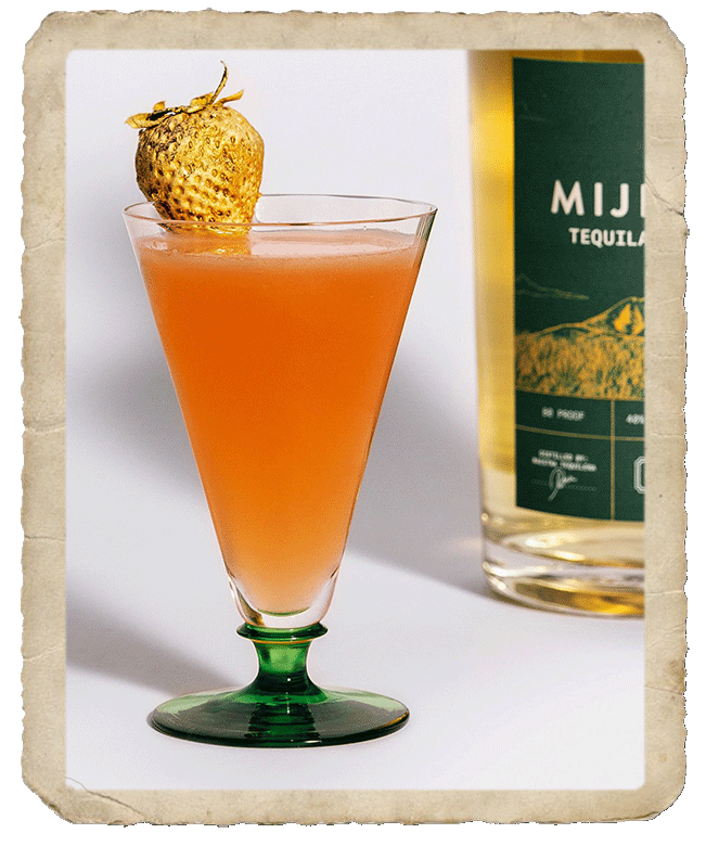 Glass cup containing the deep orange cocktail Mijenta Love Antidote, decorated with a golden strawberry..