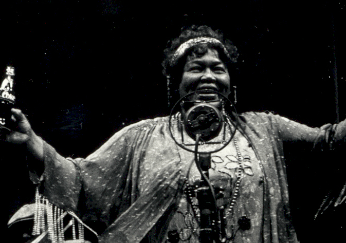 Black and white image of Ma Rainey with a big grin on her face with her arms stretched out while performing.