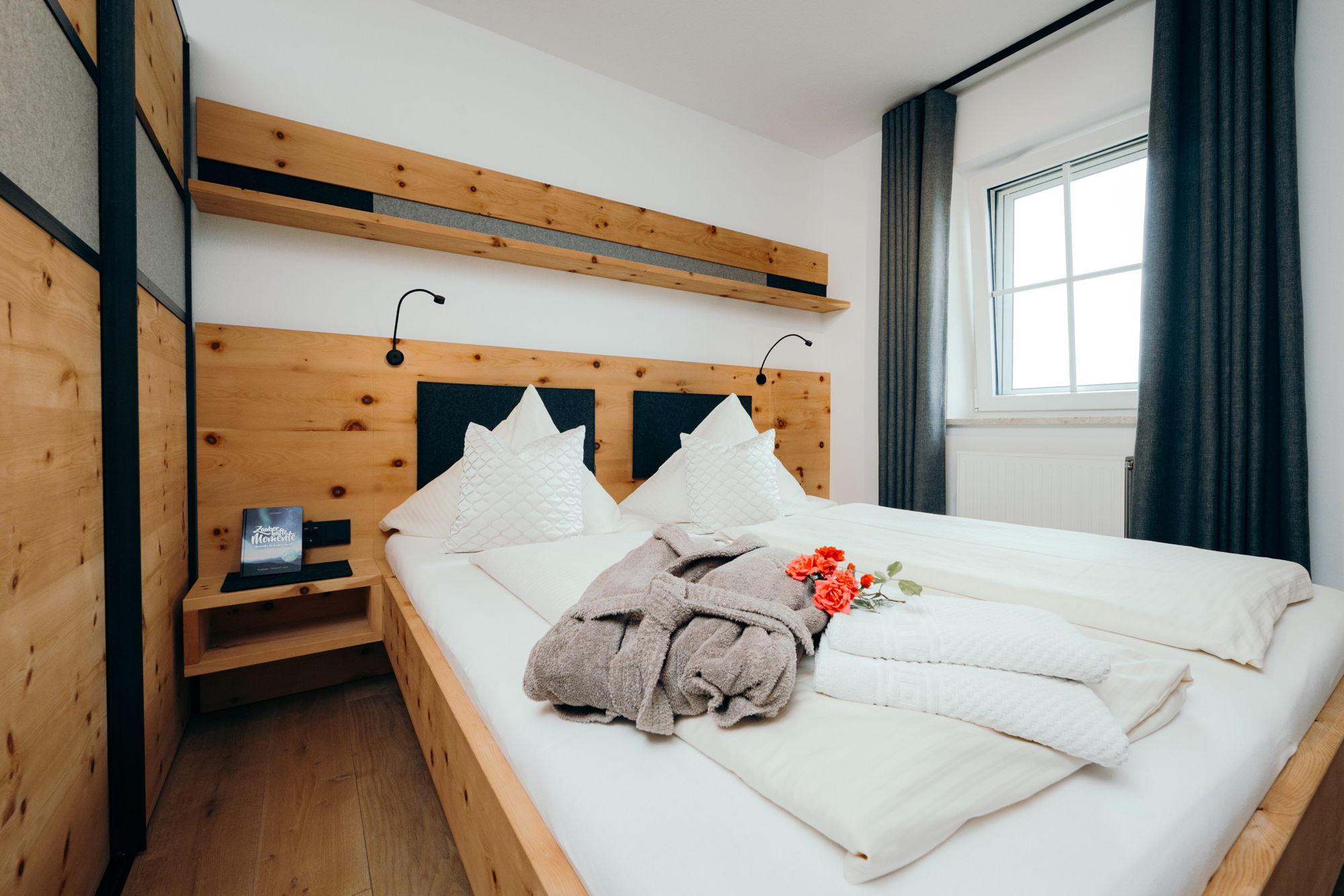 Ein mit Holz verkleidetes Schlafzimmer mit dunklen Vorhängen und einem weiß bezogenen Doppelbett.