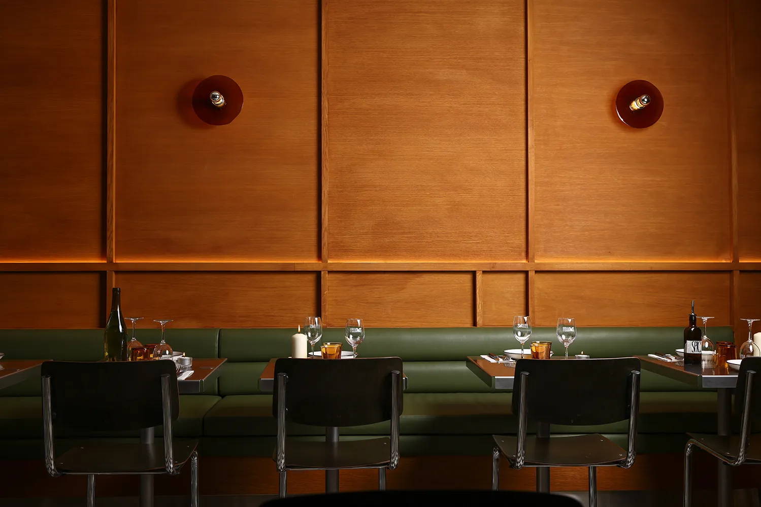 A restaurant interior showing tables and chairs connected by one large green bench and red wood wall