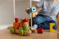 A little boy playing with a colorful Montessori wooden car toy in his playroom.