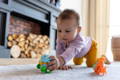 Baby girl playing with toys on a carpet next to the fireplace. 