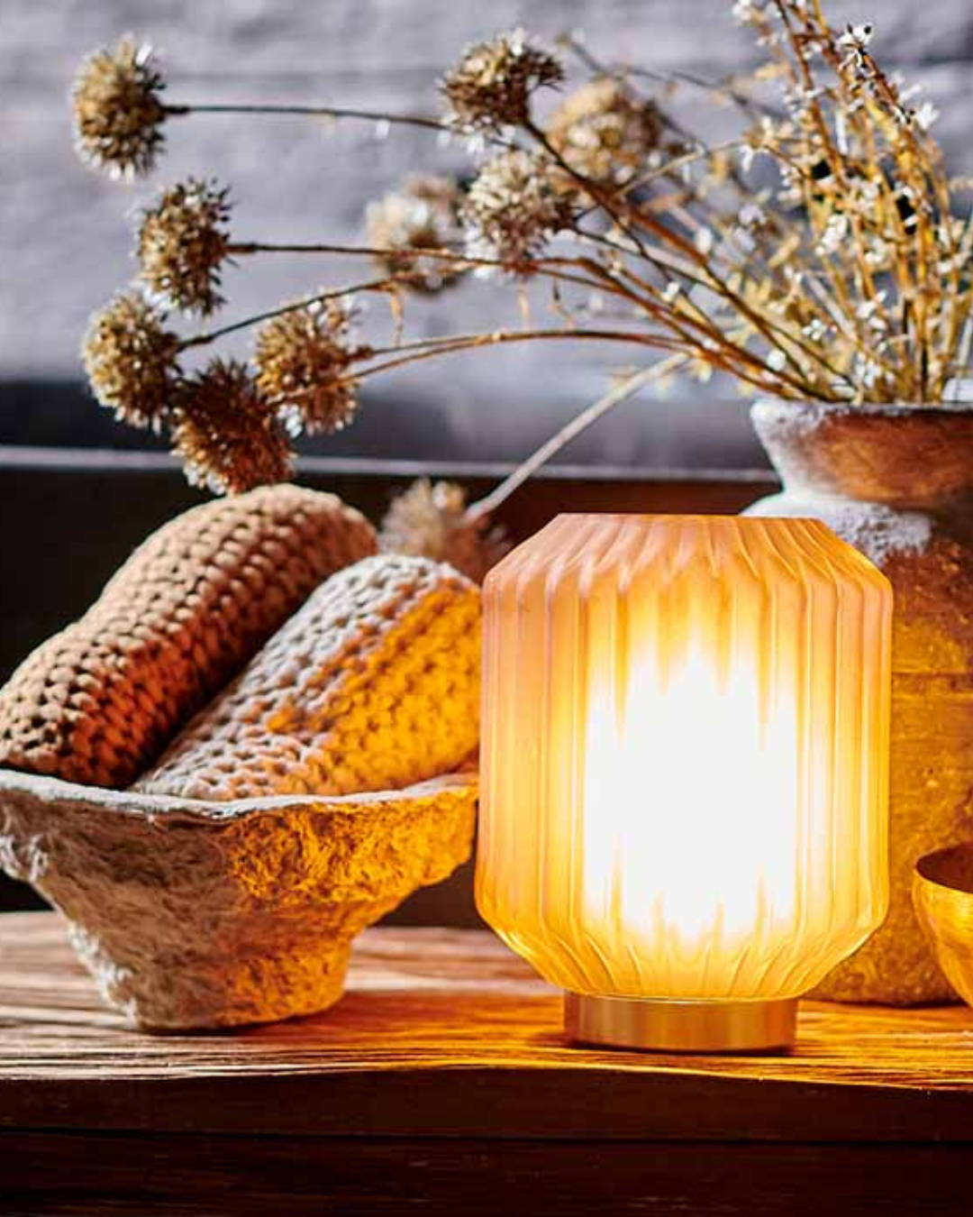 A close up of a glass LED lamp next to some dried flowers and a paper cache bowl filled with waffle textured flannels