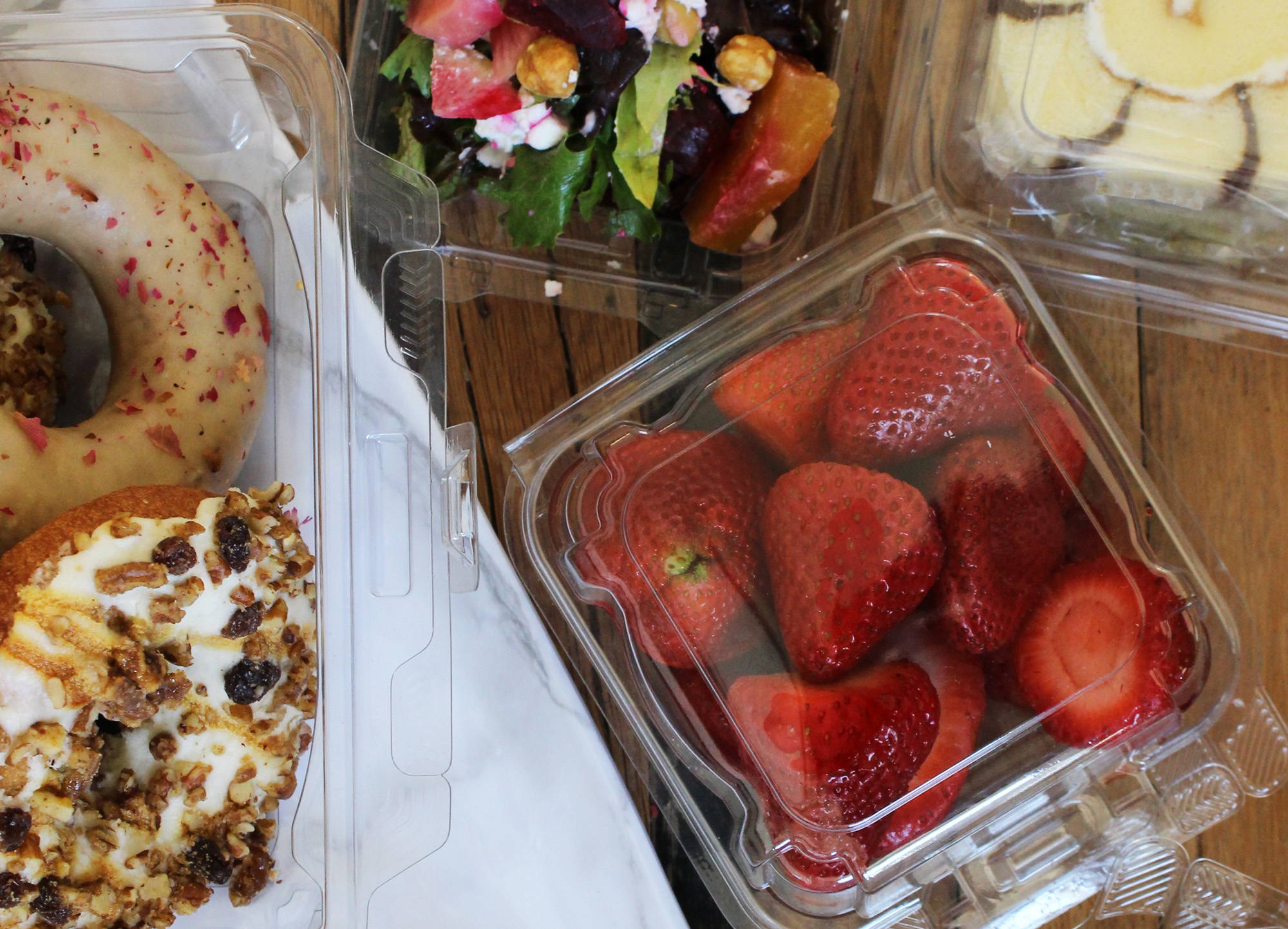 Simply Secure clamshell containers made from biodegradable bioplastic, fulled with strawberries, salad, and doughnuts