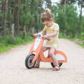 Little girl sitting on her Montessori Balance Vespa on the forest road.