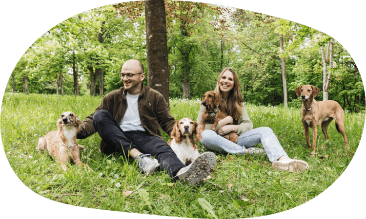 Lächelnde Frau, die kniend ihrem Hund Futter anbietet. Dahinter eine weiße moderne Küche mit großem Fenster