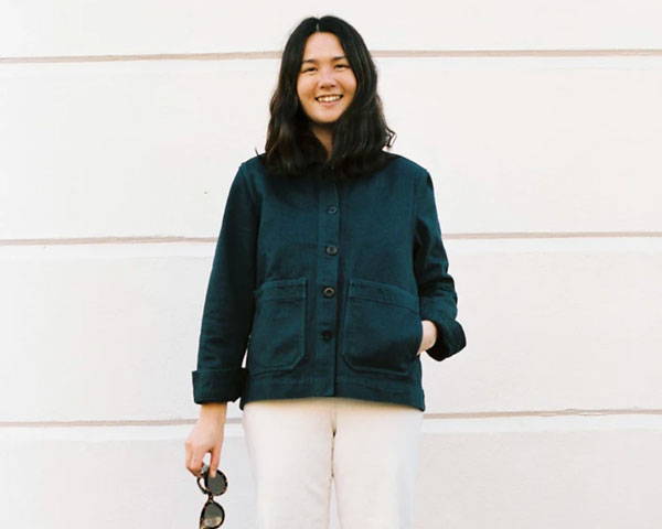 Woman wearing a navy blue chore jacket smiling with cream trousers from the sustainable clothing brand Paynter Jacket Co