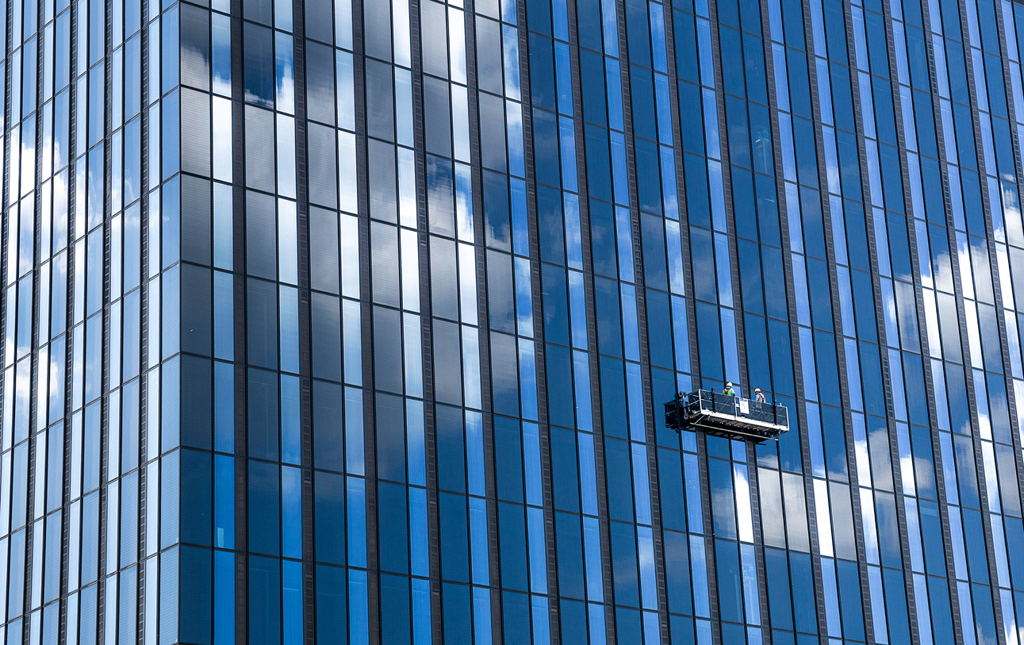 A tall skyscraper and professional high-rise window cleaning service workers in a gondola